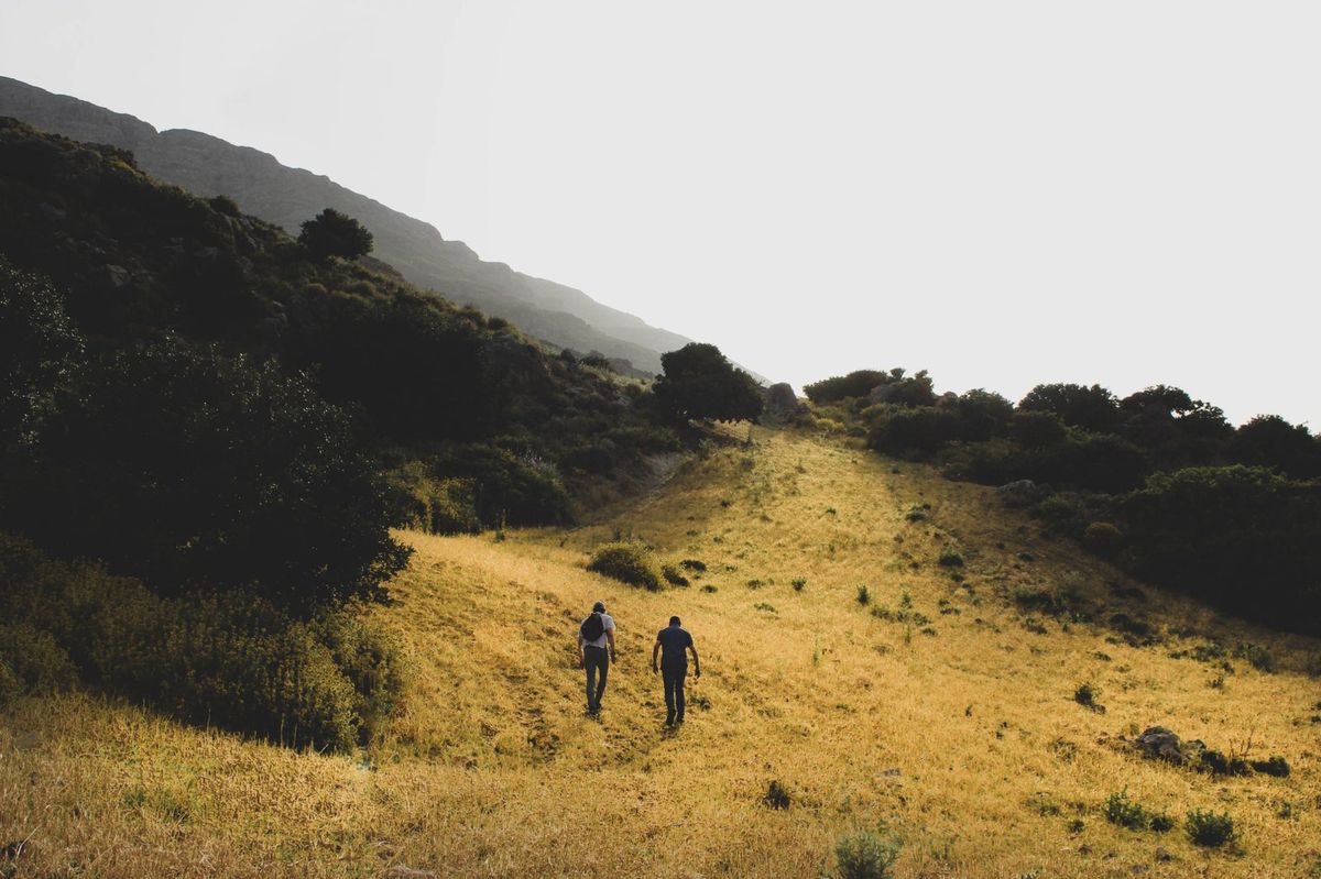 Deux personnes montent ensemble un chemin herbeux à flanc de colline, dans la lumière du soir.