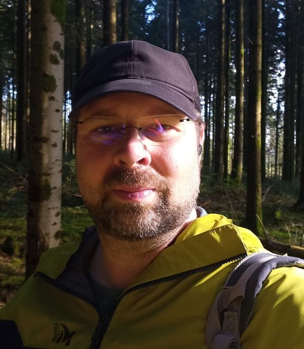 Portrait de Kévin Solinski en forêt, casquette et veste jaune, le regard tourné vers l’objectif.
